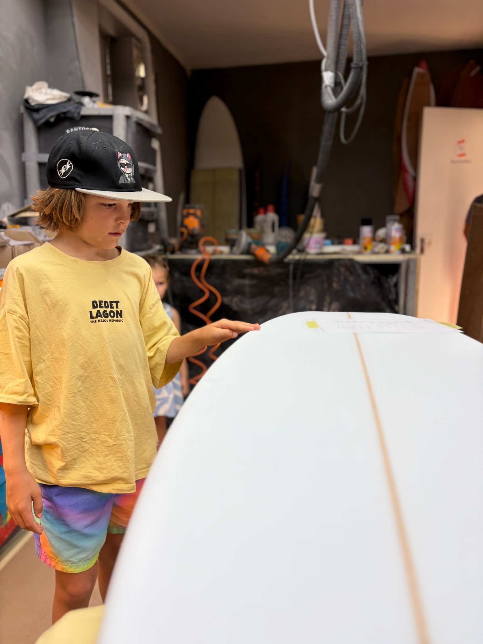 Noah sizing up the raw white blank on the shaping stand, dimensions taped to the foam