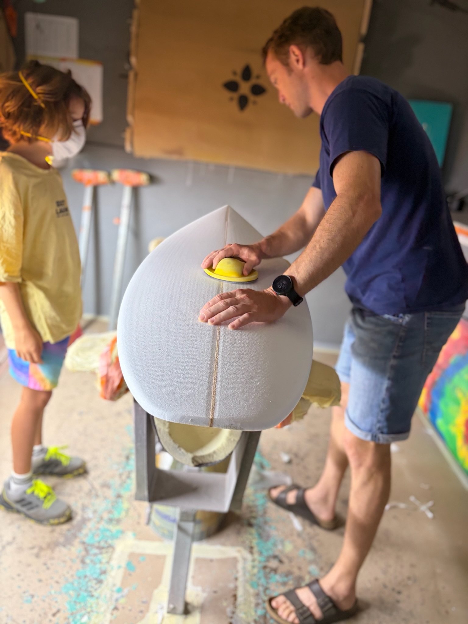 The shaper and Noah sanding the rails of the white blank together on the stand