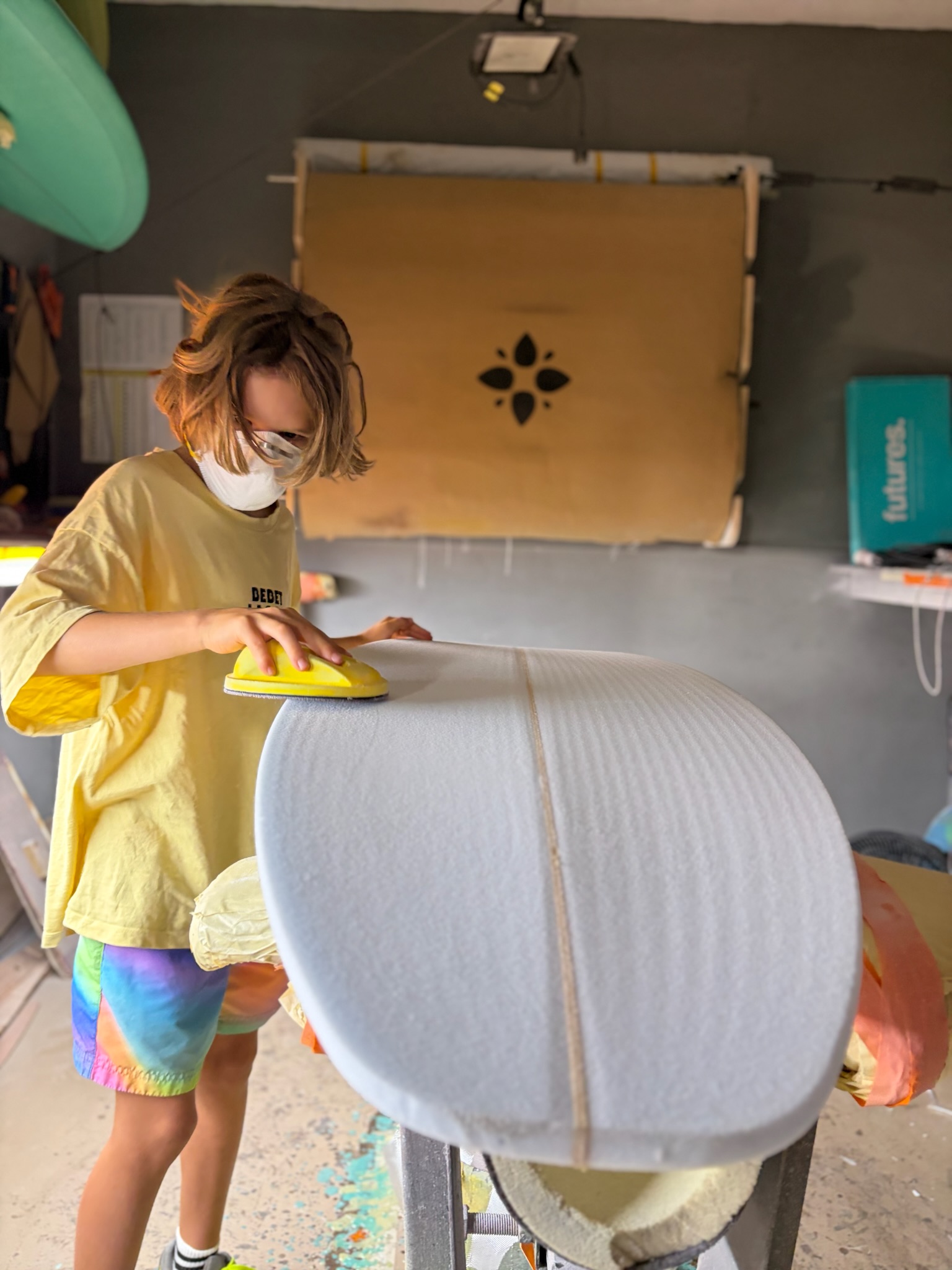 Noah sanding the deck of the blank with a yellow pad, dust mask on