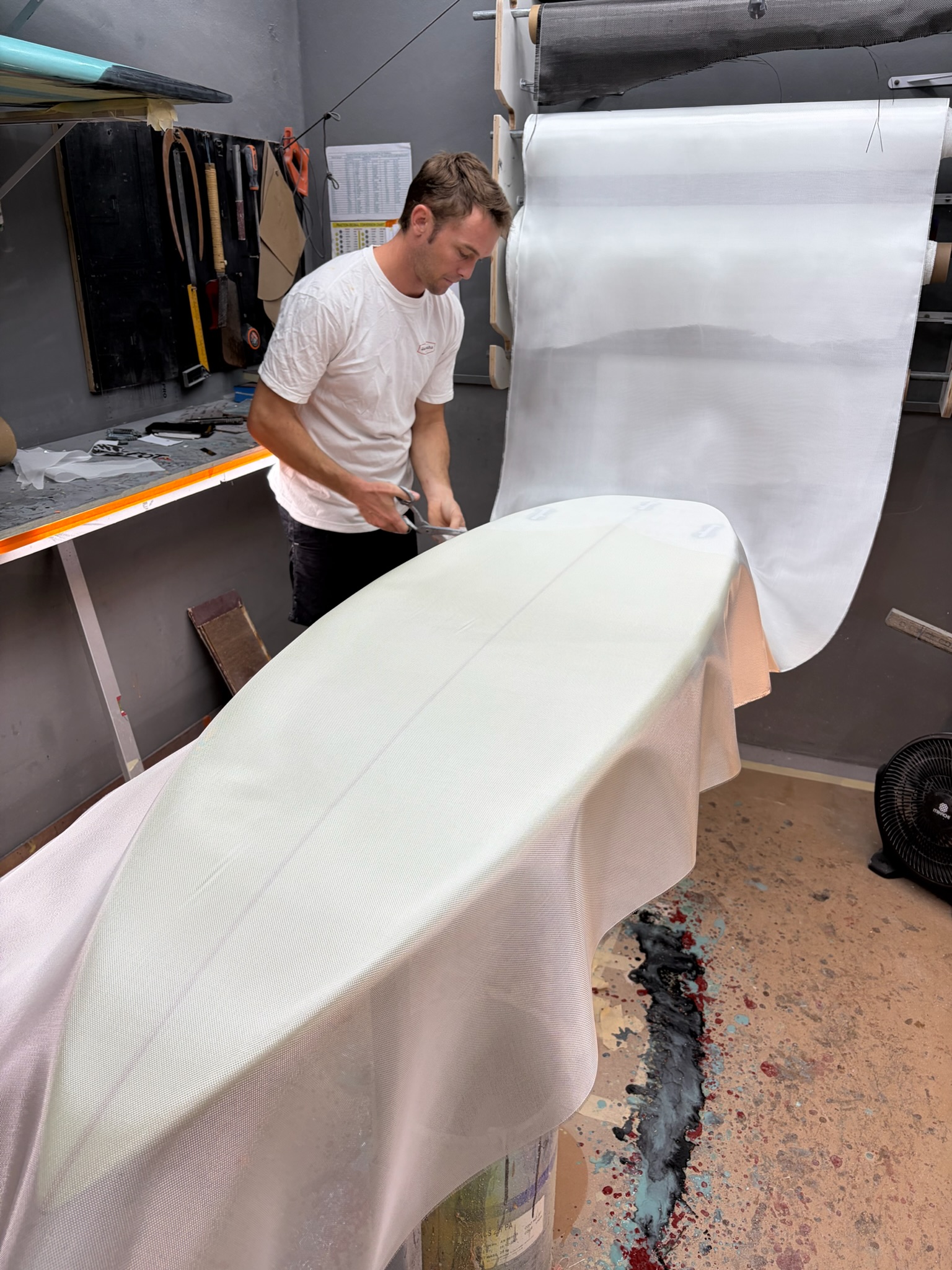A shaper laying the fiberglass cloth over the foam blank