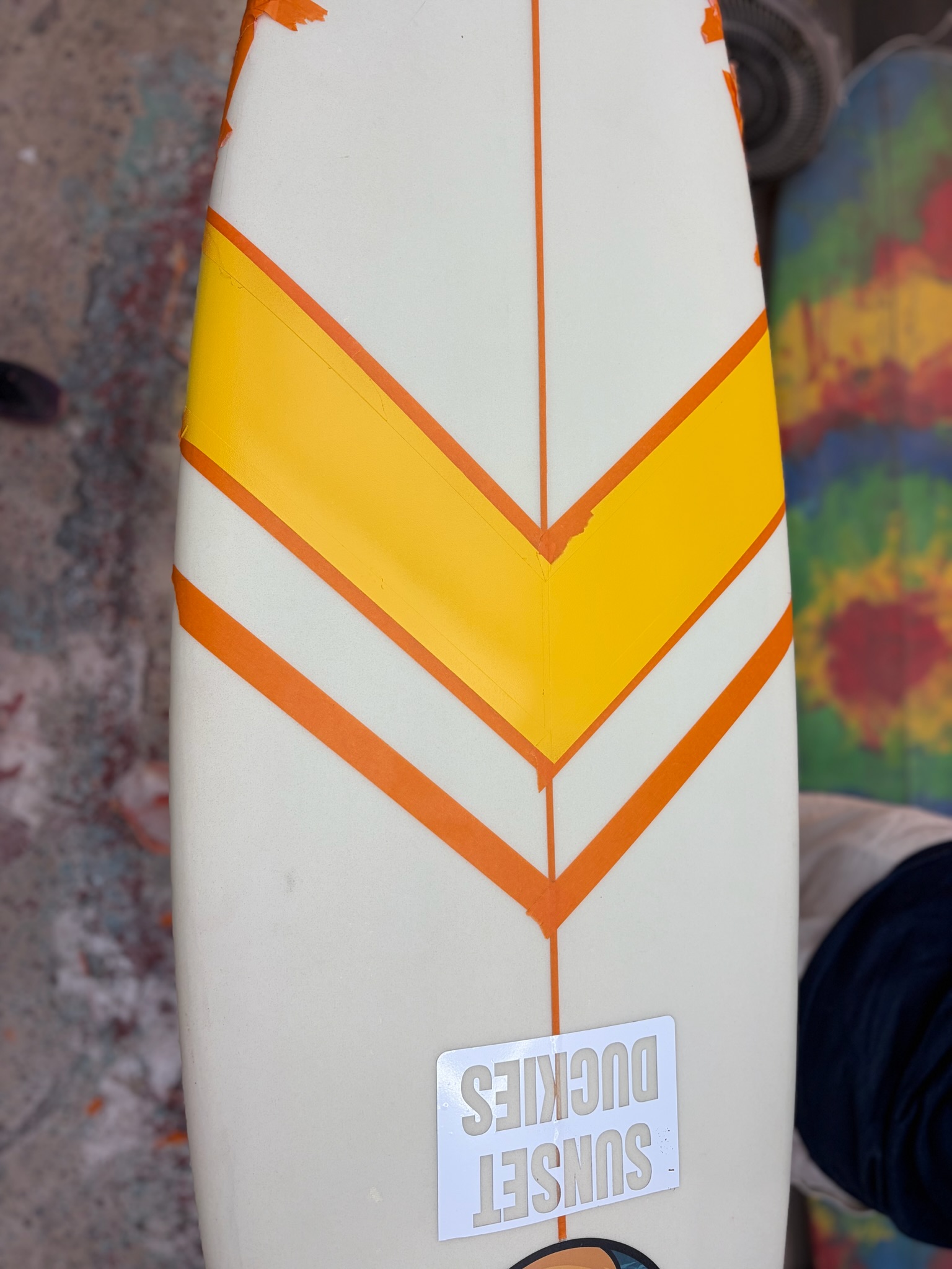 Masking the orange-and-yellow chevron on the deck stripe by stripe, Sunset Duckies sticker below