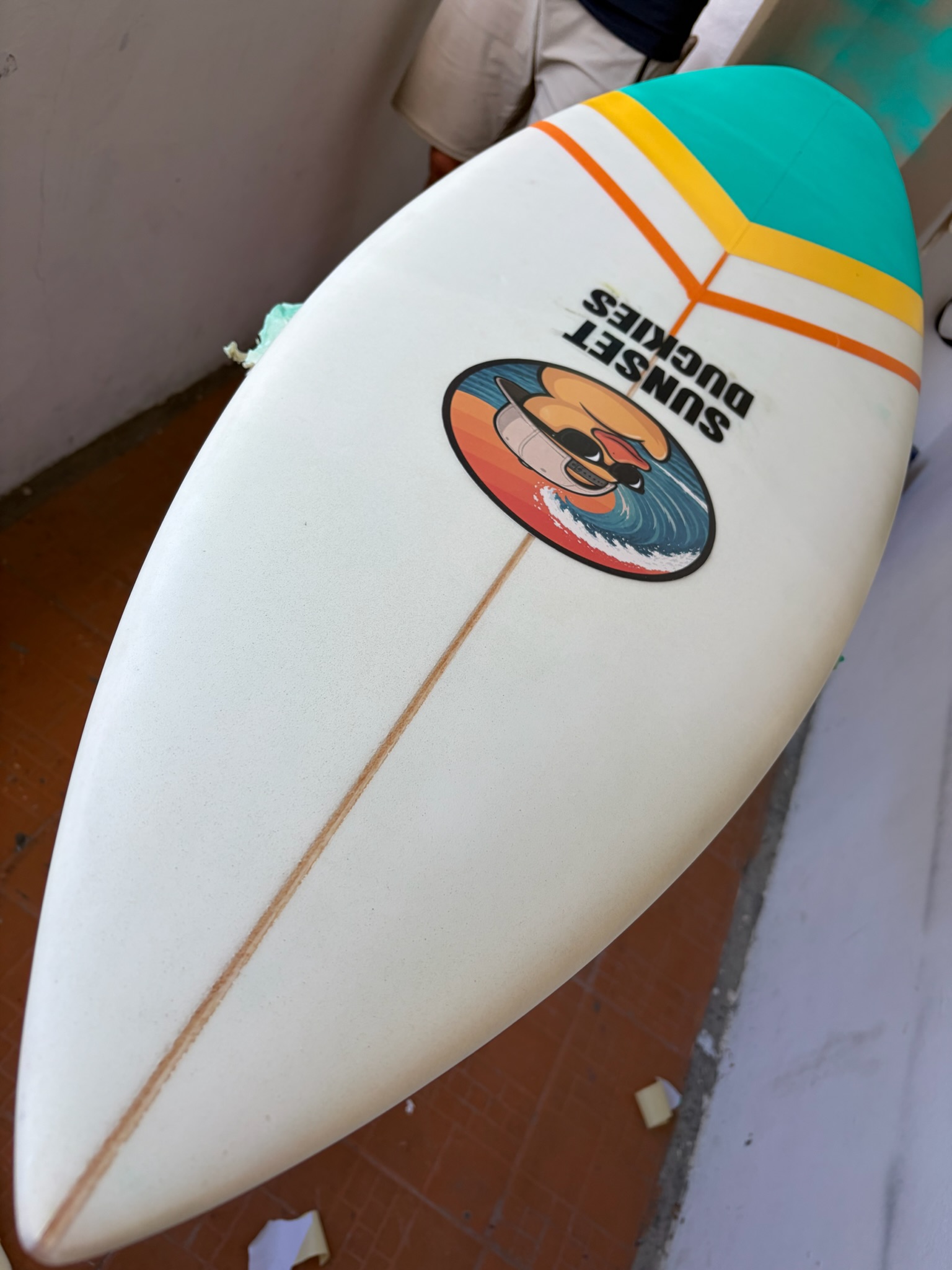 The finished board bottom: duck logo, Sunset Duckies wordmark, teal-yellow-orange chevron at the tail