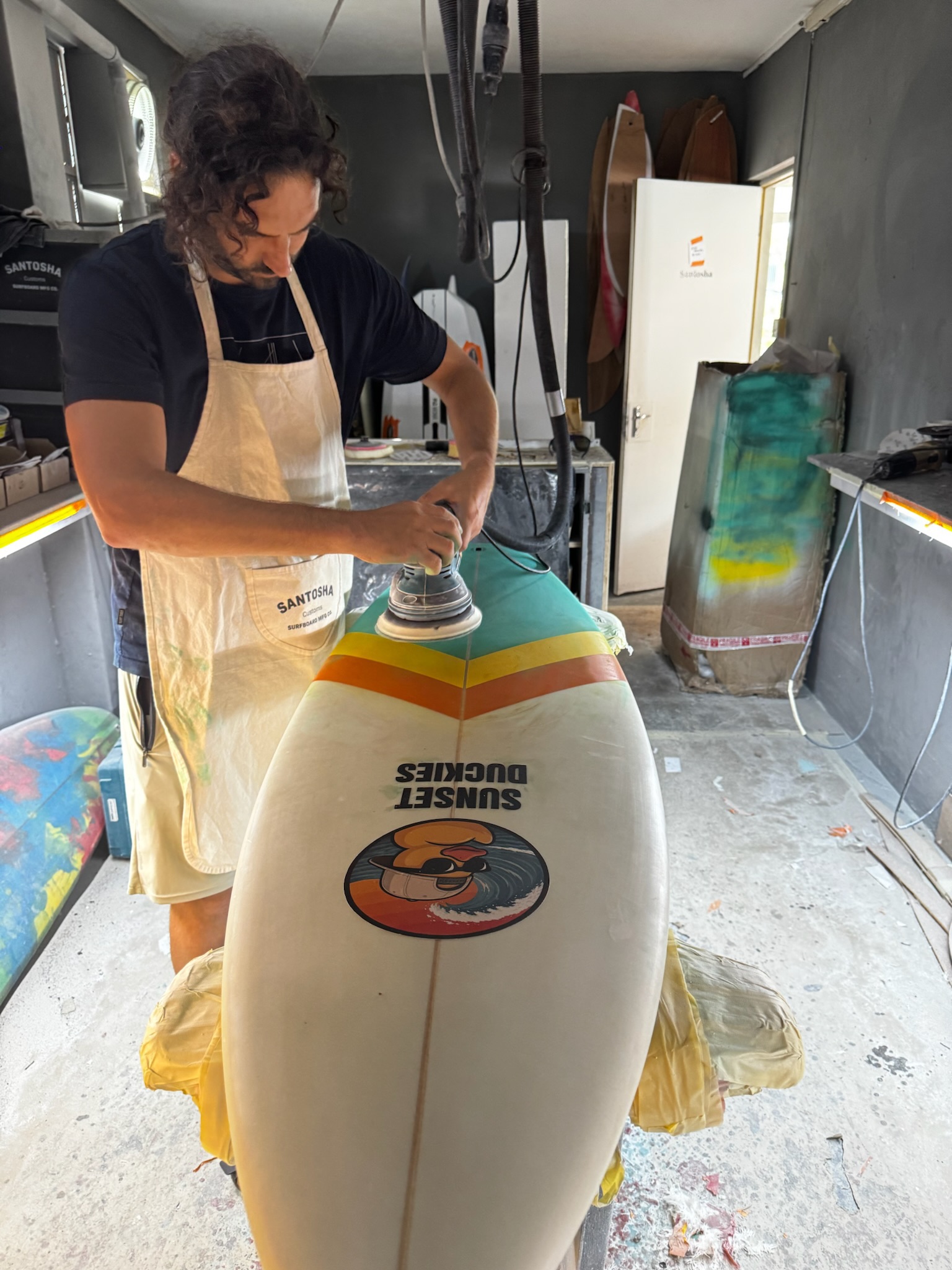 The board nose-up on the stand while a shaper finishes the deck