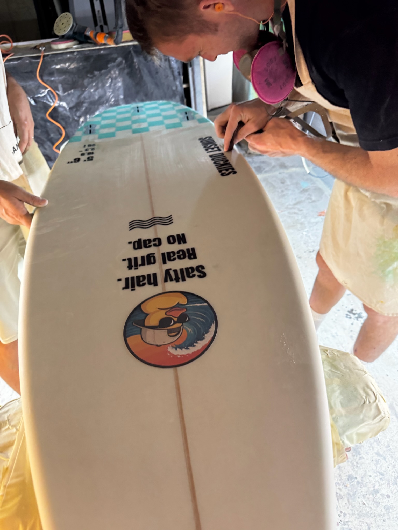Close-up of the bottom: Salty hair. Real grit. No cap. above the duck logo, dimensions near the stringer
