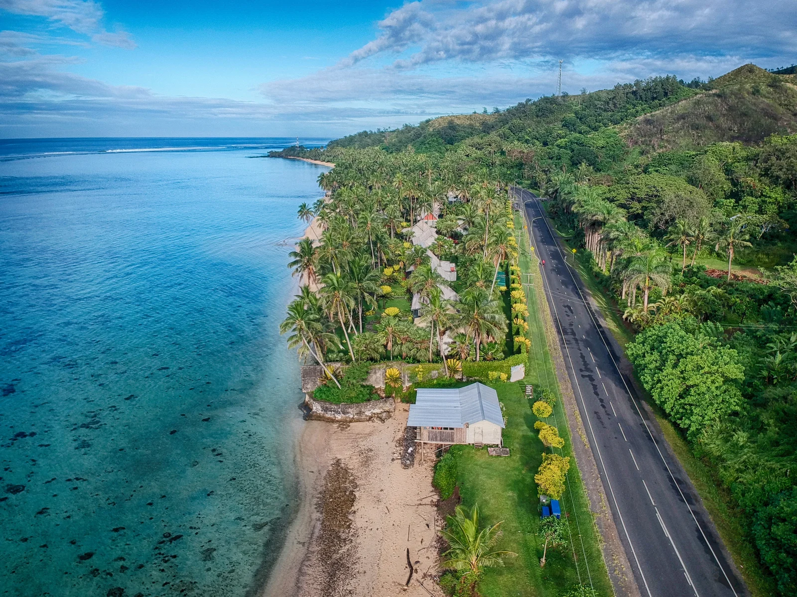 Aerial view of Queens Road along Fiji's Coral Coast, with palms and reef shallows beside the ocean.